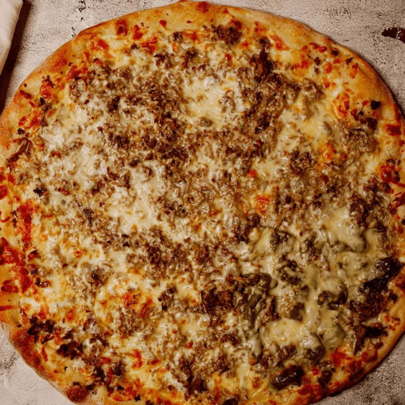 Overhead view of a whole pizza with a golden crust, melted cheese, and ground meat toppings.