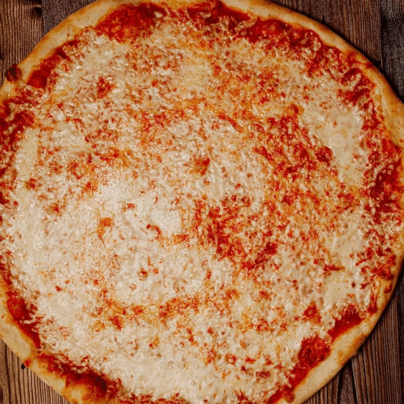 A large, round cheese pizza with a golden crust sits on a rustic wooden table.
